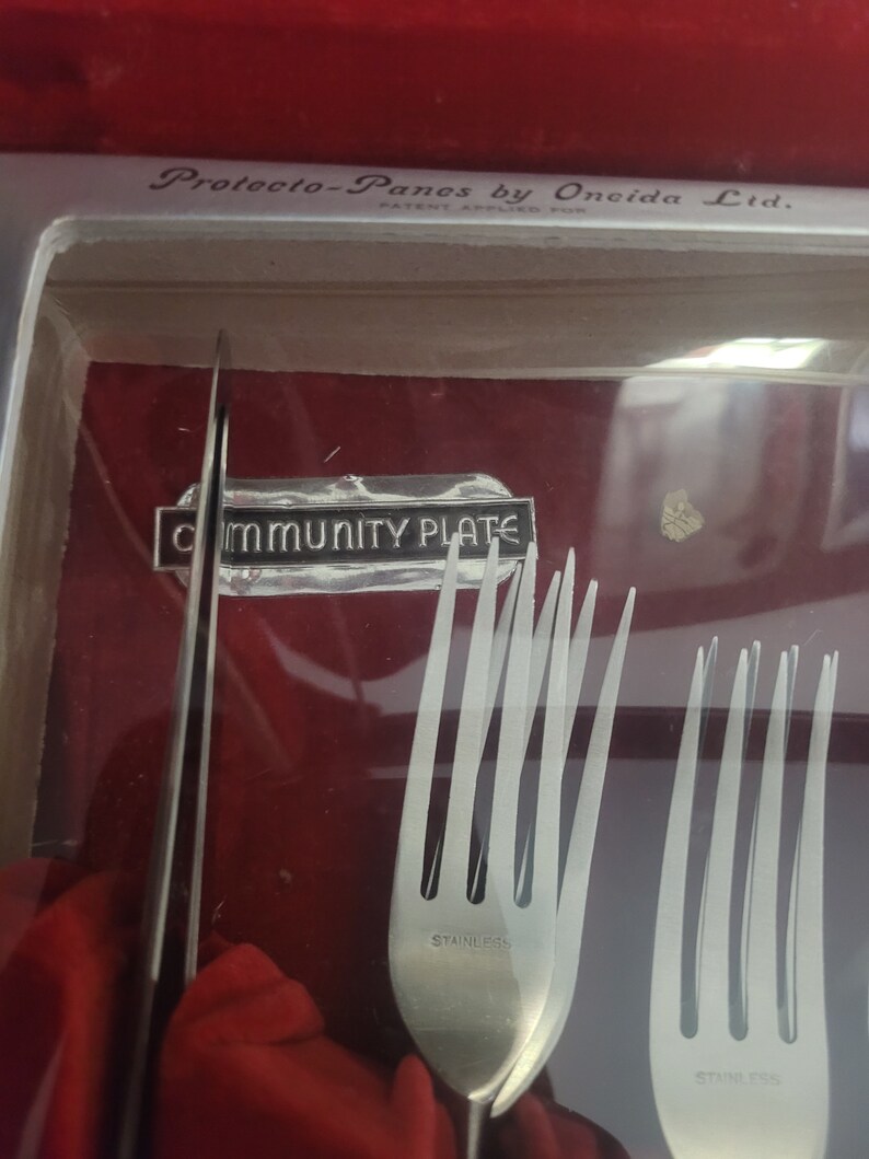 May include: A close-up of a set of silverware in a red velvet box. The silverware is marked "Community Plate" and "Stainless".