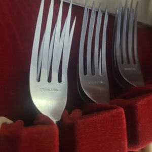 May include: Close-up of a set of silver forks in a red velvet box. The forks are labeled "Stainless" on the back.