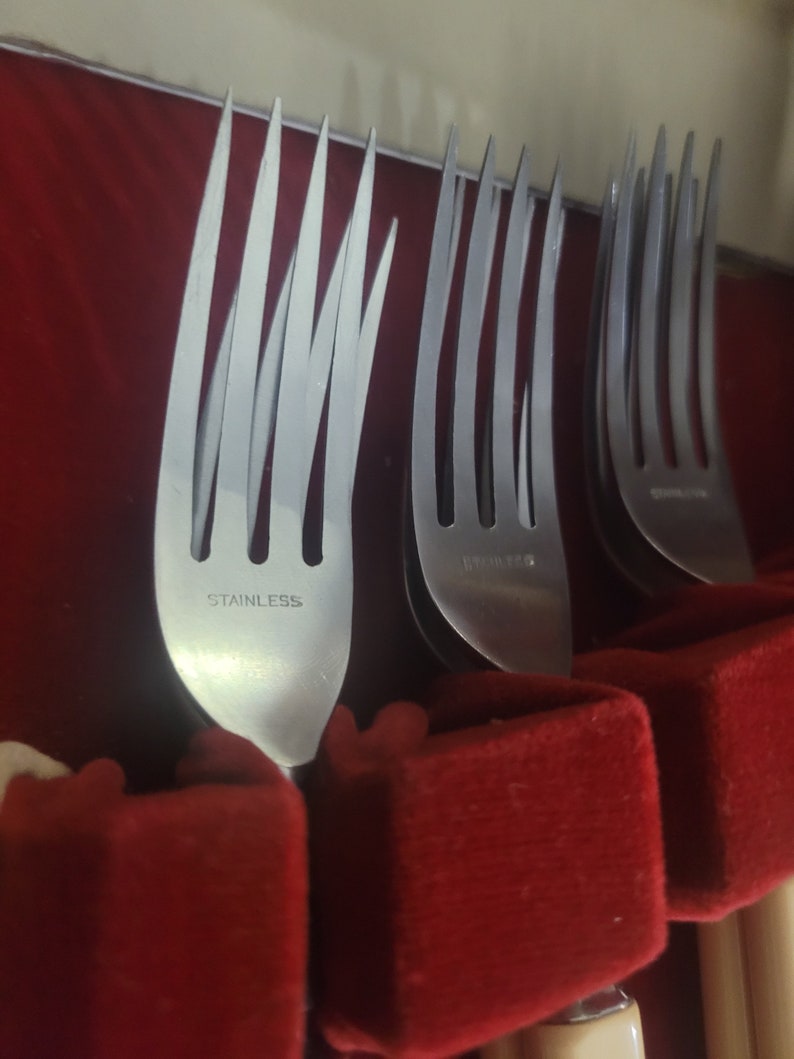 May include: Close-up of a set of silver forks in a red velvet box. The forks are labeled "Stainless" on the back.