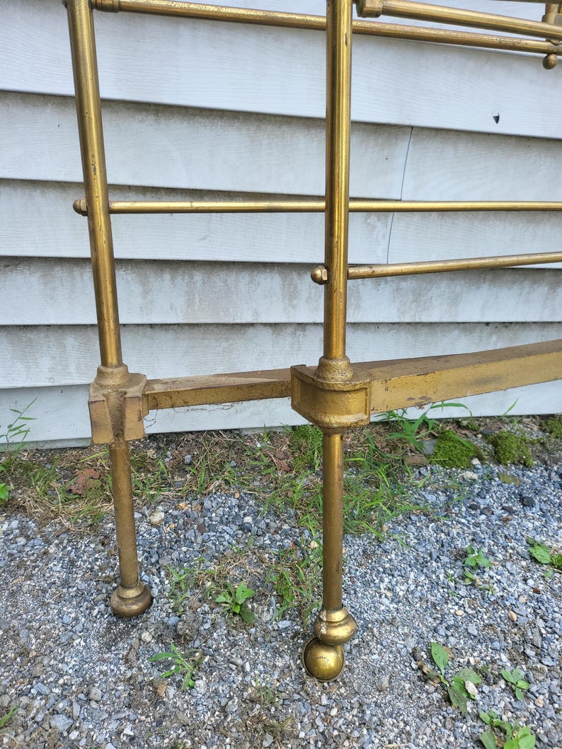 Op de afbeelding: Een vintage messing bedframe met een gouden afwerking. Het frame heeft verticale palen en horizontale staven, met decoratieve bolvormige voeten. Het bedframe is ontworpen voor een standaard matrasmaat.