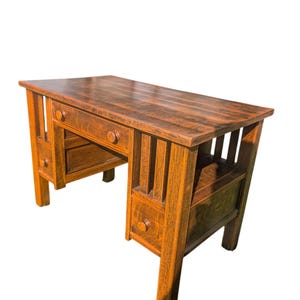 May include: A rectangular wooden desk with a dark brown finish and visible wood grain. The desk features a central drawer with a round knob, vertical slat detailing on the sides, and an open storage compartment on the right side with a small drawer.