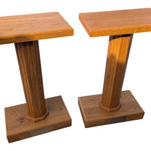 May include: Two wooden side tables with a rectangular top and a fluted column base. The tables are made of light brown wood and have a rectangular base. Each table has a small metal plaque on the base.