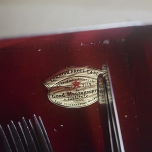 May include: A gold sticker with the text "Tarnish Proof Case" and "Tested and Approved" with a red star and the number "2149". The sticker also says "Good Housekeeping Institute" and "Good Housekeeping Magazine".