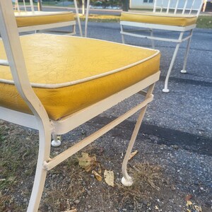 May include: White metal patio chairs with yellow cushions. The chairs have a simple, elegant design with curved legs and a woven back.
