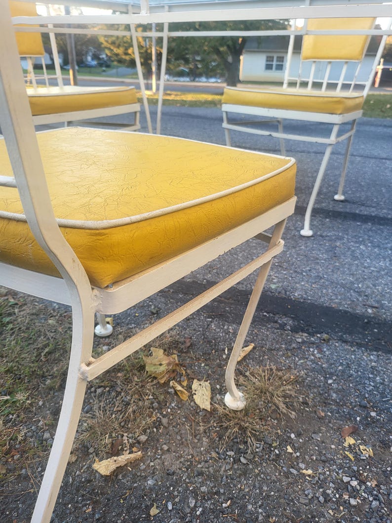 May include: White metal patio chairs with yellow cushions. The chairs have a simple, elegant design with curved legs and a woven back.