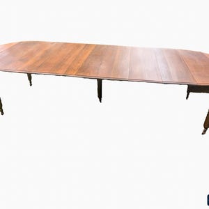 May include: A large, oval wooden dining table with a warm brown finish. The table has a planked top and is supported by turned legs. The table is approximately 96 inches long and 48 inches wide.