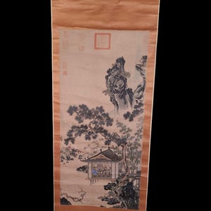May include: An antique Asian scroll painting depicting a serene landscape with a pavilion, trees, and mountains. The artwork features muted colors and traditional brushstrokes, showcasing a tranquil scene. The scroll is mounted on a brown backing.