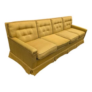 May include: A four-cushion sofa in a golden yellow hue. The sofa features a button-tufted back and seat cushions, with a skirted base. The arms are slightly angled, and the overall design is reminiscent of mid-century modern furniture.