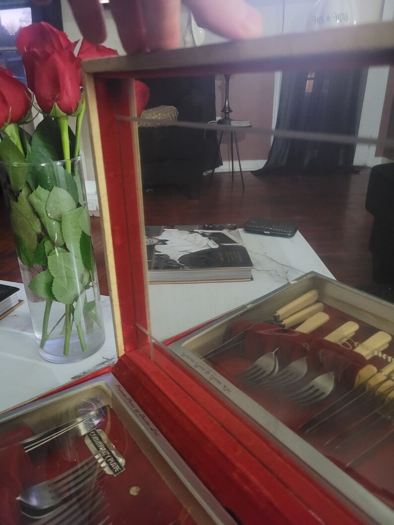 May include: A red velvet lined wooden box with a glass top, containing a set of silver Community Plate silverware. The box has the words "Community Plate" and "Stainless Steel" printed on the inside.