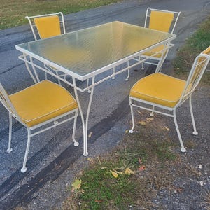 May include: A white metal patio dining set with four chairs and a glass-top table. The chairs have yellow cushions.