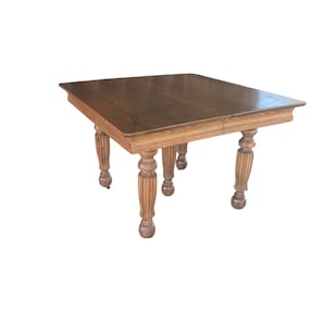 May include: A square wooden dining table with a dark brown finish and a visible wood grain pattern. The table features four thick, vertically fluted legs with rounded, bulbous feet at the base, supporting a flat, smooth tabletop surface.