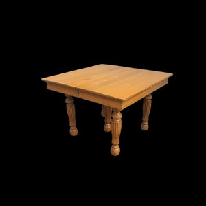 May include: A square wooden table with four turned legs. The table is made of light brown wood and has a simple design.