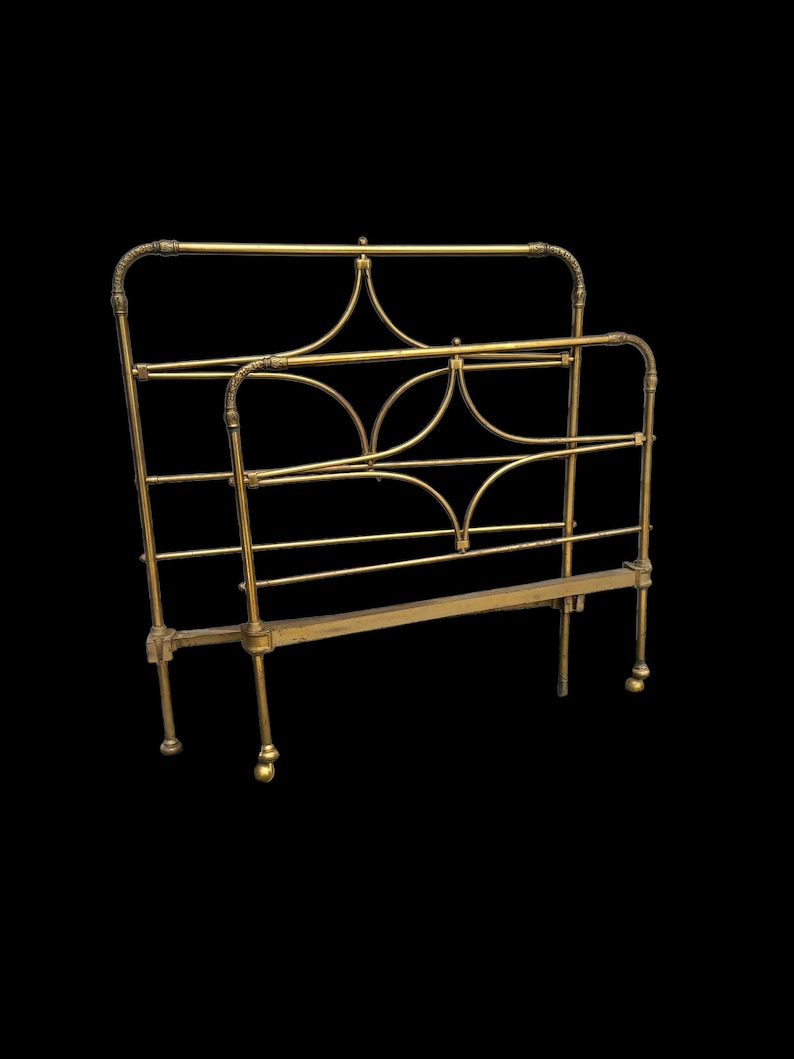 Op de afbeelding: Een vintage messing bedframe met een sierlijk ontwerp. Het hoofdbord en voetbord hebben gebogen lijnen en decoratieve accenten. Het bedframe is gemaakt van messing en heeft een warme, gouden kleur.
