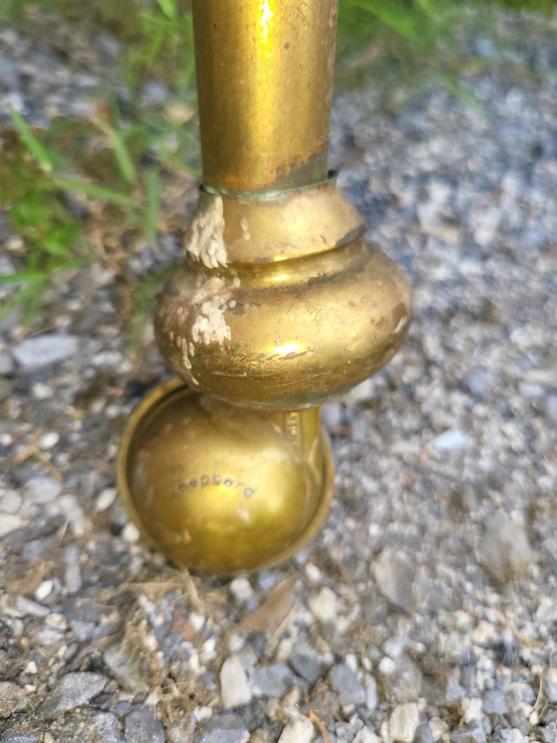 Op de afbeelding: Close-up van een messing meubelwiel met een afgeronde basis en een klein wiel. Het wiel heeft een gouden afwerking en het woord "Shepherd" is aan de zijkant gegraveerd. Het wiel is bevestigd aan een messing poot.