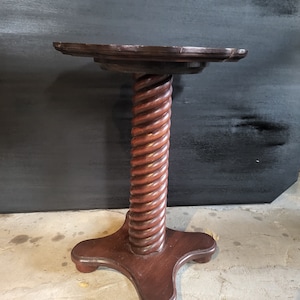 May include: A dark brown wooden side table with a round top and a twisted, rope-like pedestal base. The base has a four-pronged foot.