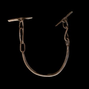 May include: A rusty metal chain with two hooks on either end. The chain is bent into a U shape.