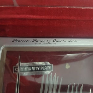 May include: A silver case with a red velvet lining. The case contains a set of silver forks with the words "Protector-Panes by Oneida Ltd. Patent Applied For" and "Community Plate" printed on the case.