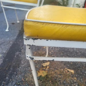 May include: Two white metal chairs with yellow cushions. The chairs have a simple, classic design and are in good condition, although there are some signs of wear and tear on the paint.