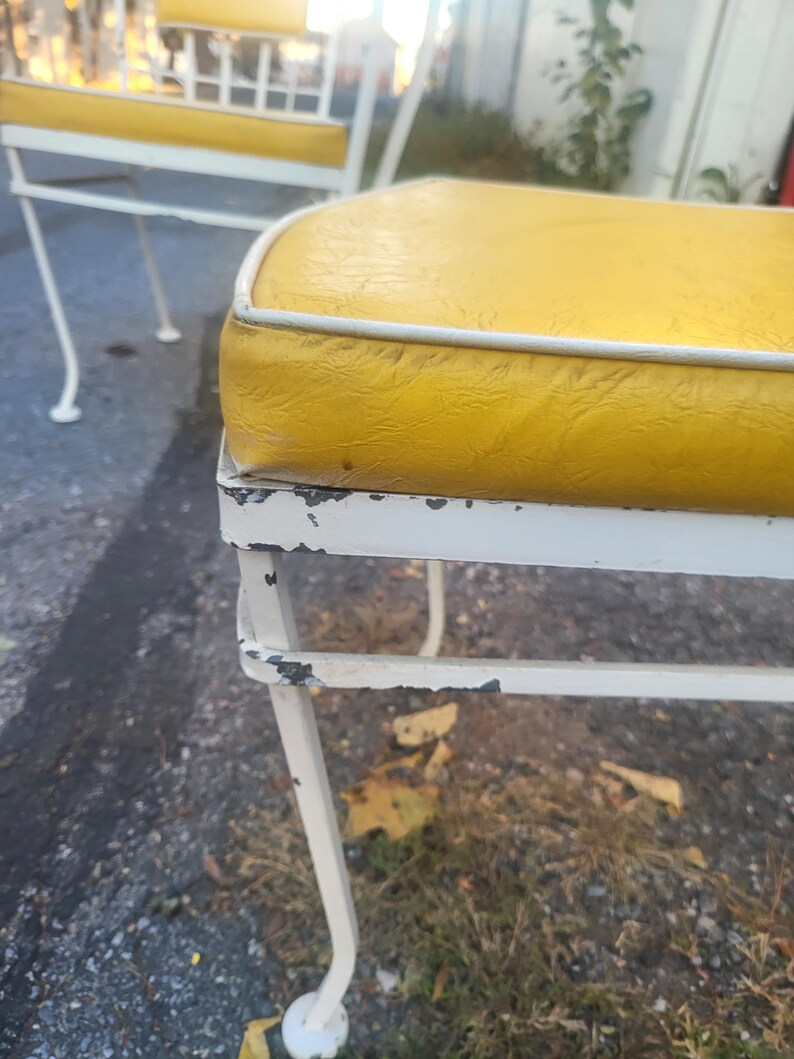May include: Two white metal chairs with yellow cushions. The chairs have a simple, classic design and are in good condition, although there are some signs of wear and tear on the paint.