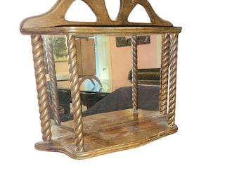 May include: A wooden wall mirror with a shelf and a rope-like design on the sides. The mirror has a beveled edge and a decorative top.