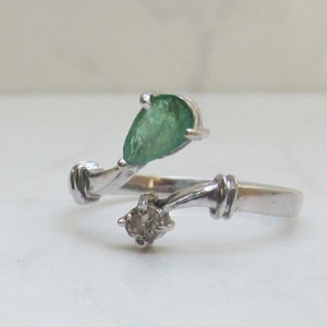 Puede incluir: Un anillo de plata con una esmeralda en forma de pera y un peque&ntilde;o diamante. El anillo est&aacute; dise&ntilde;ado con una banda retorcida.