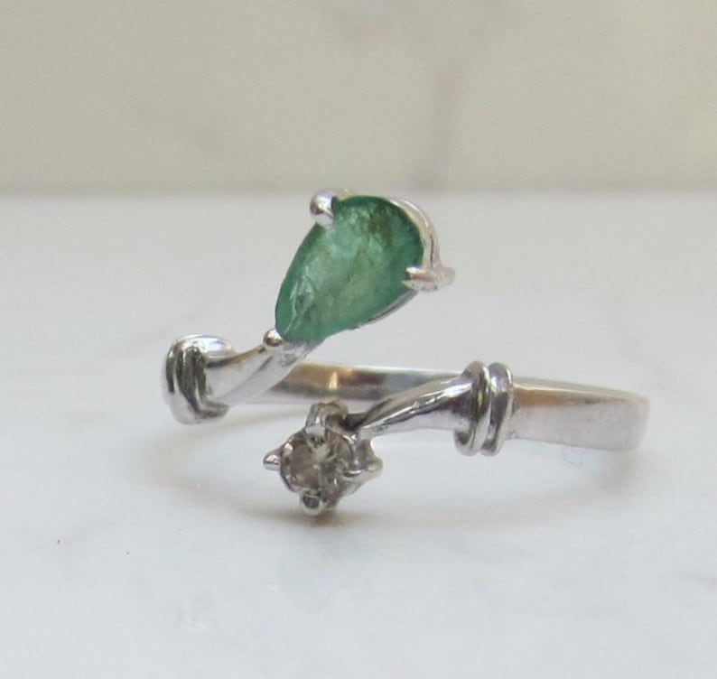 Puede incluir: Un anillo de plata con una esmeralda en forma de pera y un peque&ntilde;o diamante. El anillo est&aacute; dise&ntilde;ado con una banda retorcida.