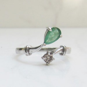 Puede incluir: Un anillo de plata con una esmeralda verde en forma de pera y un diamante redondo.
