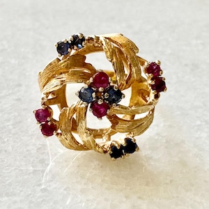 May include: A gold ring with a swirling, leaf-like design set with red rubies and blue sapphires.
