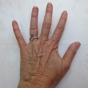 Puede incluir: Primer plano de una mano con un anillo de plata con una piedra preciosa verde. La mano est&aacute; abierta y los dedos est&aacute;n separados.