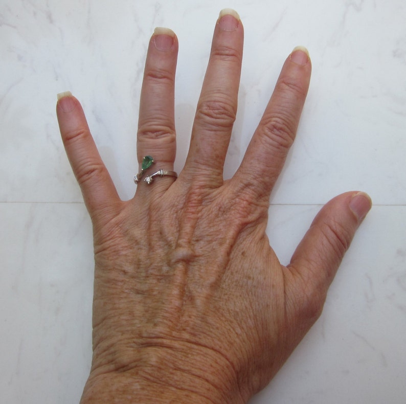 Puede incluir: Primer plano de una mano con un anillo de plata con una piedra preciosa verde. La mano est&aacute; abierta y los dedos est&aacute;n separados.