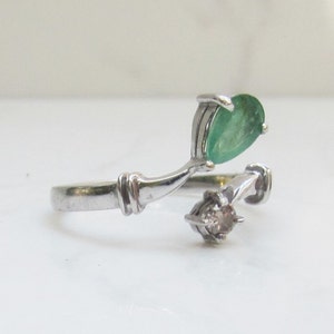 Puede incluir: Un anillo de plata con una esmeralda de forma de pera y un peque&ntilde;o diamante redondo. El anillo tiene un dise&ntilde;o &uacute;nico con la esmeralda engastada en una banda curva.