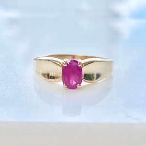 May include: A gold ring with a pink oval-shaped gemstone set in the center.