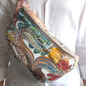 May include: A crossbody fanny pack featuring a vibrant, multi-colored abstract pattern with swirling lines, dots, and organic shapes in shades of orange, blue, yellow, and red. The bag includes a silver-toned metal zipper closure and a metal clip.