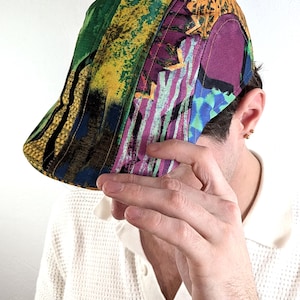 Peut inclure: Une casquette plate ornée d'un motif abstrait multicolore et vibrant, avec des nuances dominantes de vert, jaune, violet et bleu. La casquette est composée de plusieurs panneaux de tissu assemblés, présentant un design artistique audacieux.