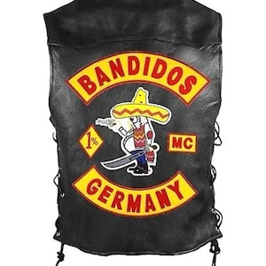 Op de afbeelding: Zwarte leren vest met een Bandidos MC-patch. De patch toont een cartoonfiguur met een sombrero die een pistool en een zwaard vasthoudt, met de woorden "BANDIDOS" en "GERMANY" in geel en rood.