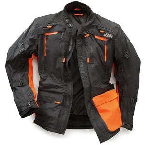 Può includere: Giacca da moto nera con dettagli arancioni. Presenta multiple tasche, cerniere e cinghie regolabili. La giacca ha il logo KTM e la scritta "READY TO RACE". Un capo di abbigliamento esterno pratico ed elegante.