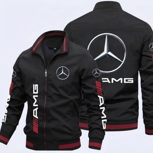 Könnte beinhalten: Schwarze Jacke mit Reißverschluss und rotem und weißem AMG-Branding. Die Jacke hat das Mercedes-Benz-Logo auf der Vorder- und Rückseite. Die Jacke hat einen Stehkragen und rote Akzente an Ärmeln und Saum.