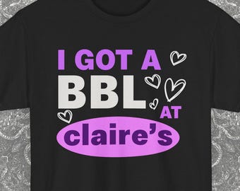 May include: Black t-shirt with the text "I GOT A BBL AT claire's" in purple and white, with heart graphics. The text is centered on the front of the shirt. A Blackash Records logo is in the bottom right corner.