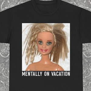 Può includere: T-shirt nero con una bambola con capelli biondi spettinati e la scritta bianca "MENTALLY ON VACATION". La bambola ha gli occhi blu e il rossetto rosa. La maglietta ha un girocollo e maniche corte. Il logo Blackash Records è in basso a destra.