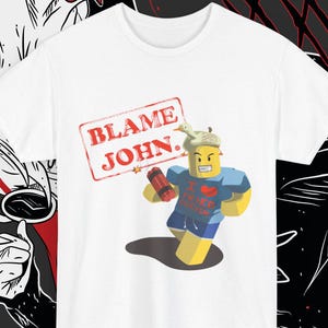 Puede incluir: Camiseta blanca con un personaje de dibujos animados y un sello rojo que dice "BLAME JOHN". El personaje sostiene un objeto rojo y lleva una camiseta azul con un diseño de corazón. Una prenda casual.