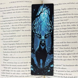 May include: A rectangular bookmark featuring a stylized illustration of a stag in a forest. The stag is black with large antlers, set against a backdrop of a blue and teal forest scene. The bookmark is placed on a book.
