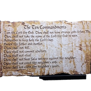 Puede incluir: Un pergamino decorativo con los Diez Mandamientos. El texto está impreso sobre una superficie similar al pergamino, con extremos cilíndricos marrones ornamentados. El pergamino está montado sobre una base negra, ideal para exhibir.