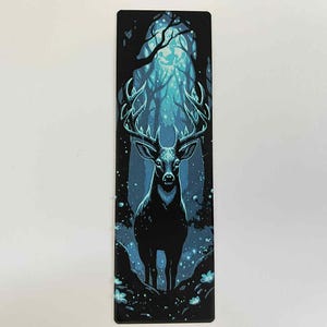 May include: A rectangular bookmark featuring a stylized illustration of a stag in a forest. The stag is black with large antlers, set against a backdrop of a blue and teal forest scene. The bookmark is approximately 2 inches wide and 6 inches tall.