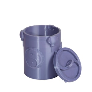 Op de afbeelding: Een lavendelkleurige cilindrische container met een deksel, met reliëfontwerpen van een Yin Yang-symbool en Chinese lantaarns. Het deksel is gedeeltelijk open en onthult de binnenkant. De container is gemaakt van een stevig materiaal.