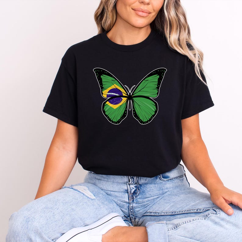 Puede incluir: Camiseta negra con un dise&ntilde;o de mariposa. Las alas de la mariposa son verdes con contornos negros, y el centro de las alas muestra los colores de la bandera brasile&ntilde;a: amarillo, azul y verde. La camiseta es de estilo casual.