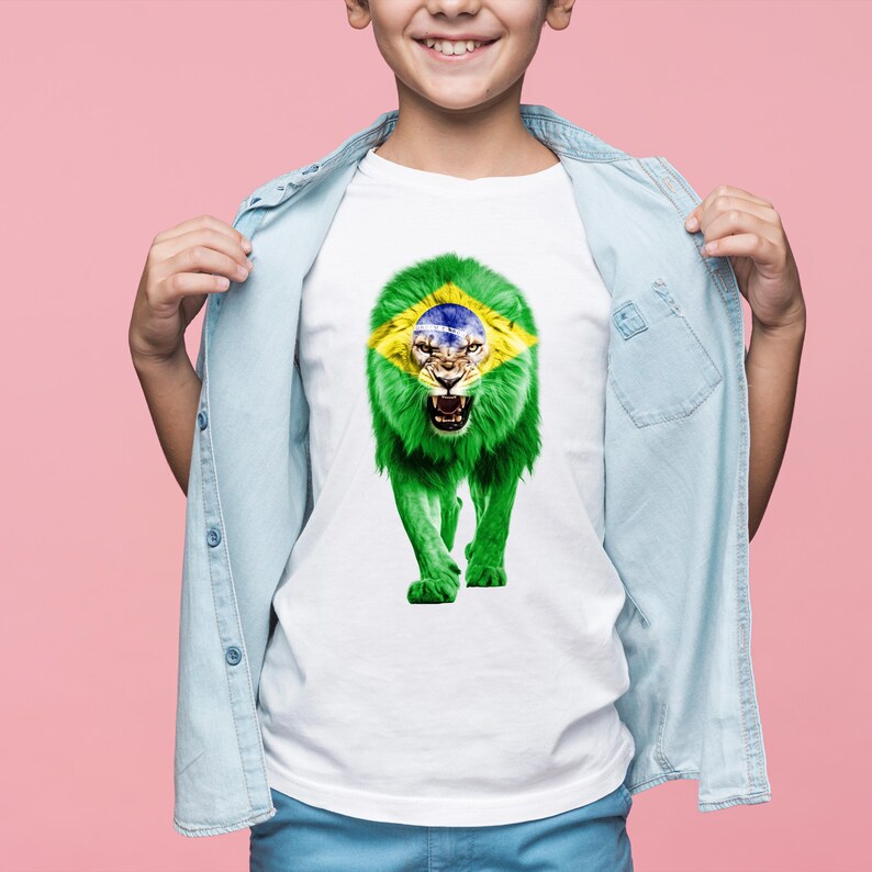 Puede incluir: Camiseta blanca con un dise&ntilde;o de le&oacute;n rugiente, con la melena y la cara del le&oacute;n que incorporan los colores y el dise&ntilde;o de la bandera brasile&ntilde;a. El le&oacute;n es verde, amarillo, azul y blanco. La camiseta la lleva una persona.