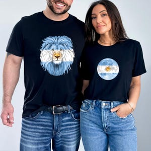 May include: Black t-shirts featuring designs related to Argentina. One shirt displays a lion with the Argentinian flag colors, while the other showcases a circular design with the flag's emblem. Both shirts are paired with blue jeans.