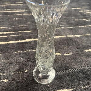Könnte beinhalten: Eine klare Glasvase mit einem geschliffenen Glasdesign. Die Vase hat einen runden Boden und einen hohen, schlanken Hals.