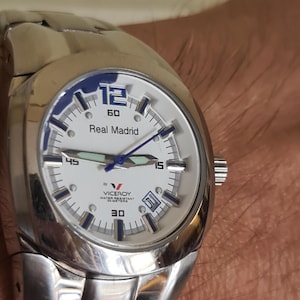 May include: Silver-toned Viceroy watch with a white face and blue accents. The watch face displays the text "Real Madrid" and "Viceroy Water Resistant 50 Meters". The watch has a date display at the 3 o'clock position and a silver-toned band.