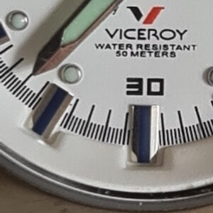 May include: Close-up of a white Viceroy watch face. The watch features black and blue hands, a black minute track, and the text "WATER RESISTANT 50 METERS". The number "30" is prominently displayed.